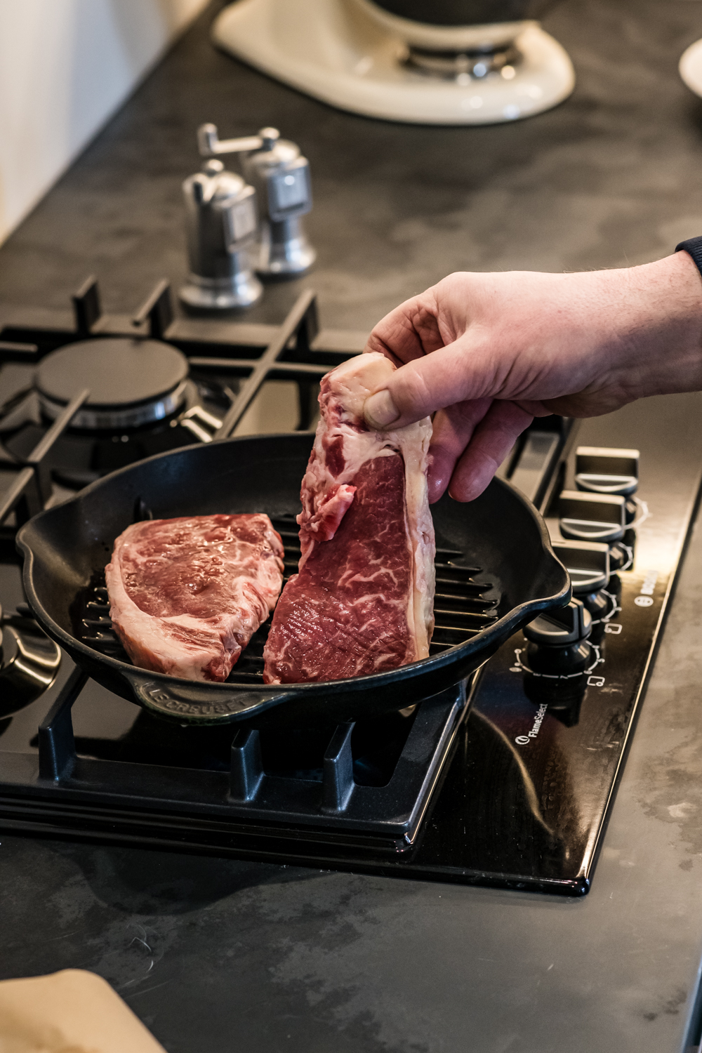 Aged ribeye steak being placed in a cast iron pan